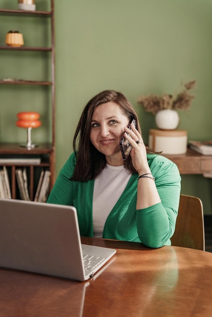 De vrouw gebruikt een laptop en een telefoon en werkt op afstand thuis als freelancer op internet