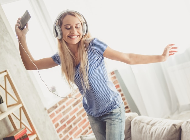 De vrouw gebruikt een smartphone, glimlacht en danst thuis