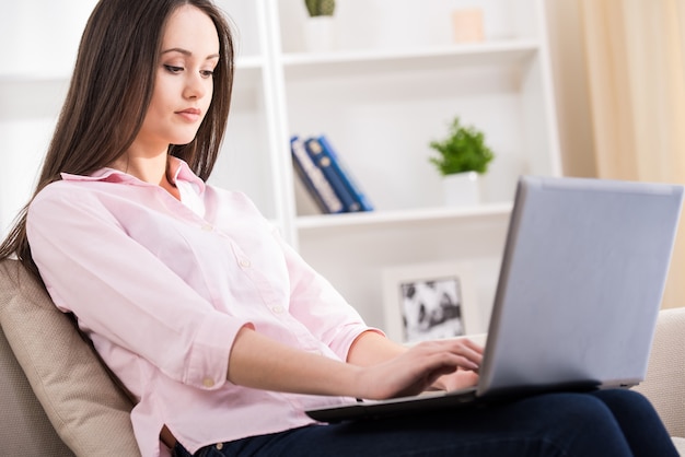 De vrouw gebruikt laptop thuis terwijl het zitten op laag.