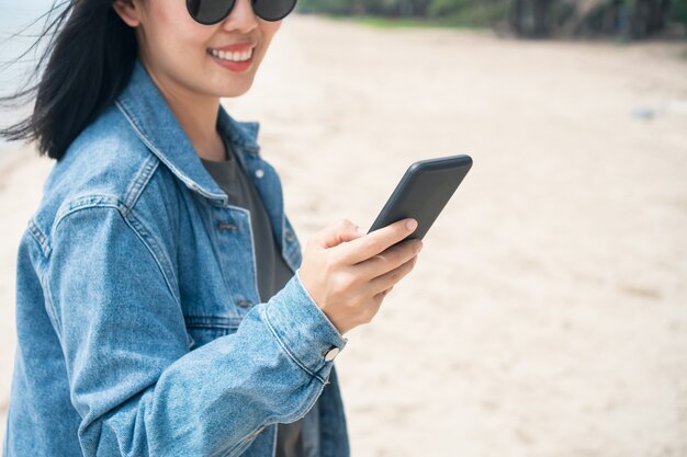 De vrouw glimlacht en gebruikt smartphone bij strand.