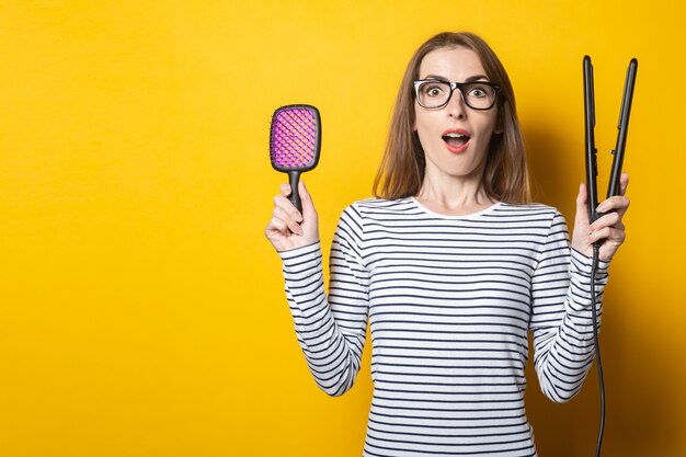 De vrouw houdt een kam en haarkrulspelden op een gele achtergrond