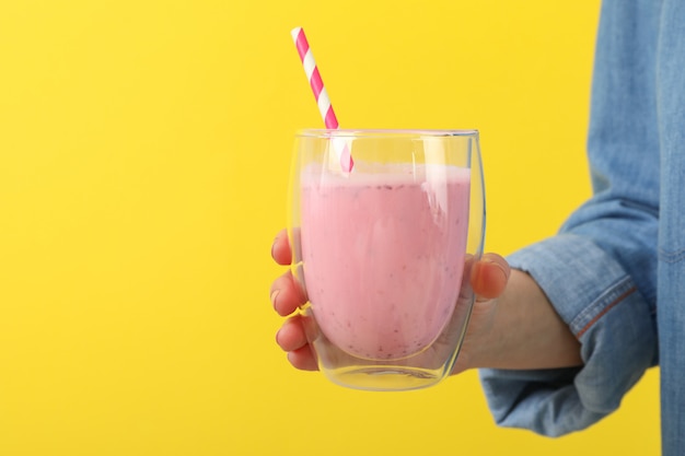 De vrouw houdt glas aardbeimilkshake tegen geel