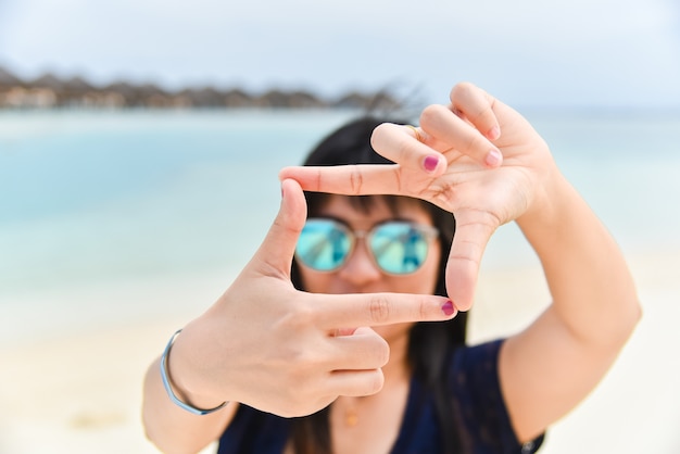 De vrouw houdt handenkader voor gezicht op het strand in de Maldiven