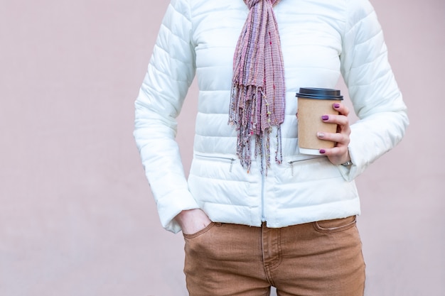 De vrouw houdt koffie in bruine kartonkop met zwart glb op roze muur