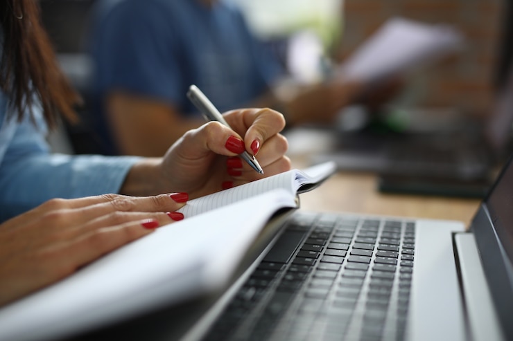 Foto de vrouw in bureau zit bij bureau en maakt nota's in notitieboekje. bedrijf