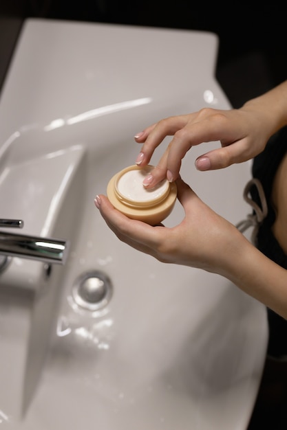 De vrouw in de badkamer pakt de crème uit de pot op haar vingers. Huid zorg concept.