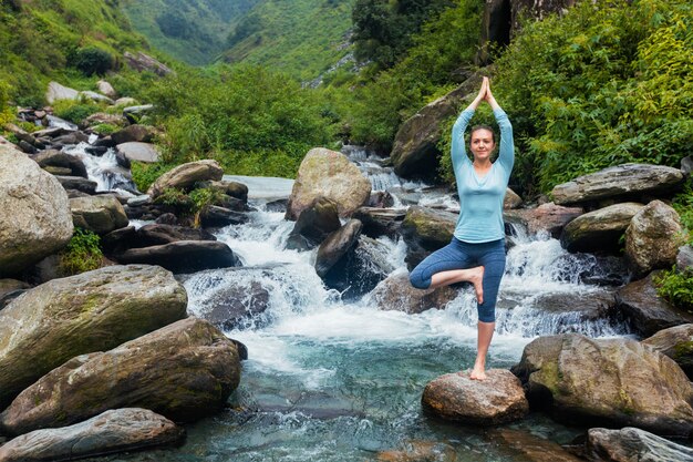 De vrouw in de boom van Vrikshasana van yogaasana stelt in openlucht bij waterval