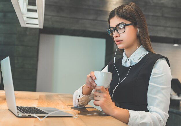 De vrouw in oortelefoons zit met de moderne laptop aan tafel