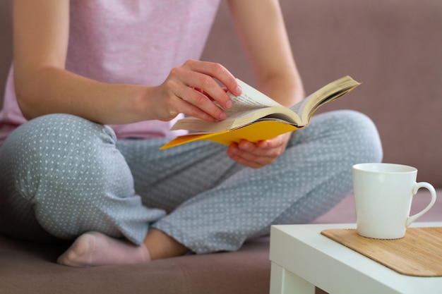 De vrouw in pyjama rust en leest thuis een favoriet boek. Gezellig tijdverdrijf