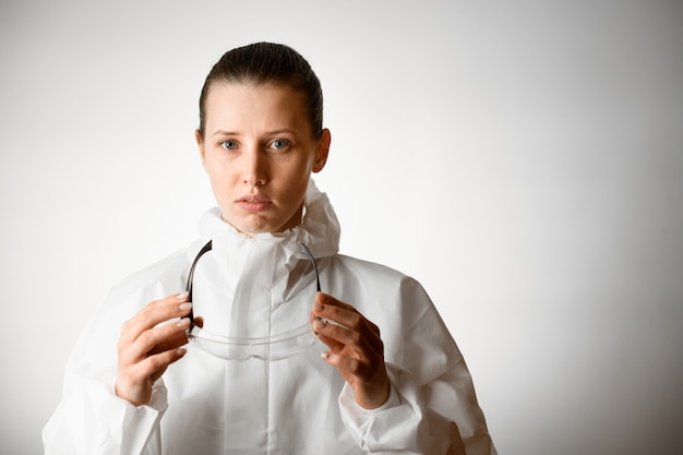 De vrouw in wit beschermend kostuum houdt beschermende glazen in haar handen.