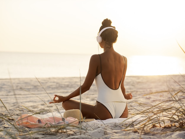 De vrouw in Yogameditatie stelt met Hoofdtelefoons op het Strand