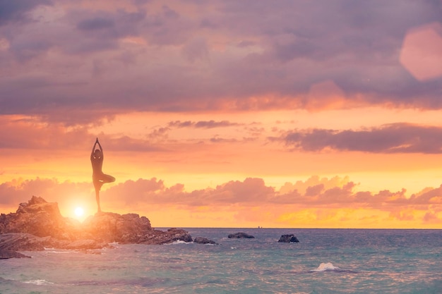 De vrouw is bezig met yoga op een achtergrond van rotsen, de zee en de lucht