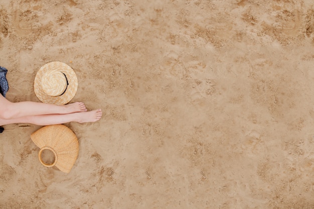 De vrouw looide benen, strohoed en zak op zandstrand. reizen concept. ontspannen aan het strand, met je voeten op het zand.