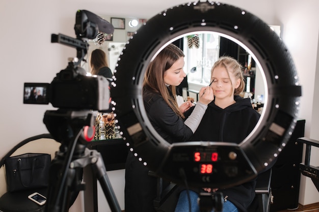 De vrouw maakt make-up voor aantrekkelijke blonde haarvrouw in studio.