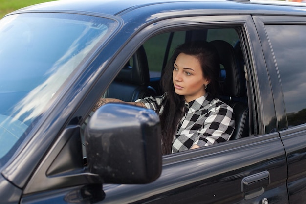 De vrouw met coole tatoeage zit achter het stuur van een auto en kijkt op de weg.