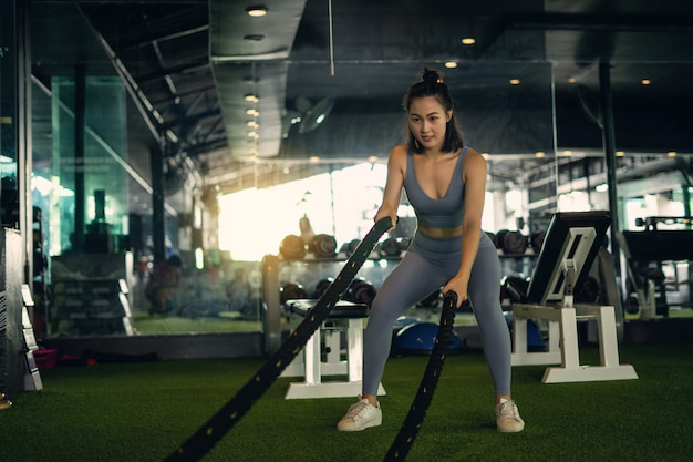 De vrouw met de slagkabels van de slagtouw oefent in de fitness gymnastiek uit.