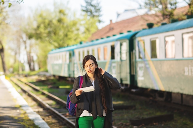 De vrouw met een rugzak, dichtbij de trein controleert zijn kaartje aan het postplatform