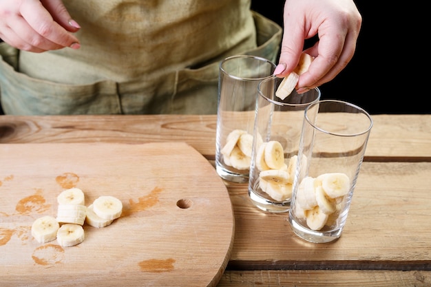 De vrouw met haar hand doet de stukjes banaan in drie lege glazen glazen