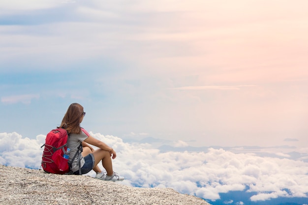 De vrouw met rugzak zit in de bergmist in de zomer bij zonsondergang