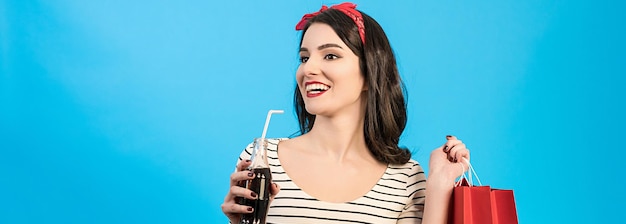 De vrouw met tassen die een cola drinkt op de blauwe achtergrond