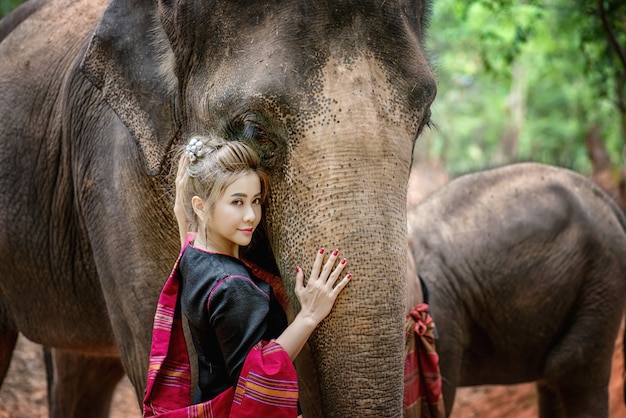 De vrouw met traditionele Thaise kleding koestert haar olifant, bij olifantendorp, Surin, Thailand