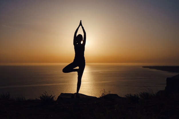 De vrouw met yogahouding op de berg bij zonsondergang.