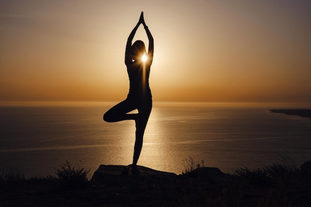 De vrouw met yogahouding op de berg bij zonsondergang.