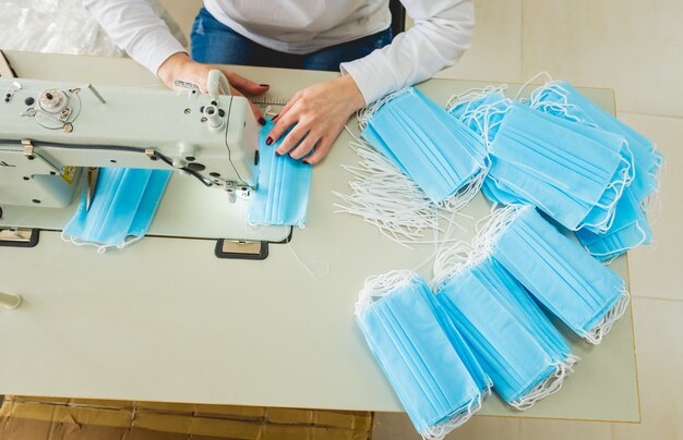 De vrouw naait gezichts medisch bij naaimachine. Coronavirus pandemie.