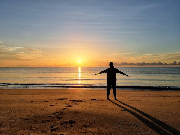 De vrouw oefent op het strand tijdens zonsopgang in de vroege ochtend