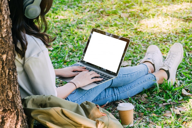 De vrouw ontspant en gebruikt een laptop computerzitting op gras in park