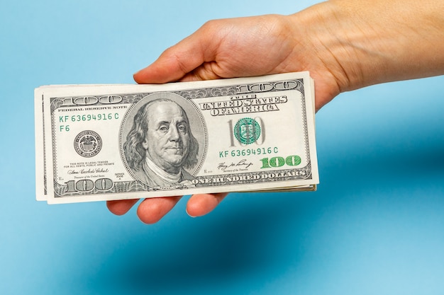 De vrouw overhandigt tellende dollarbankbiljetten op blauw