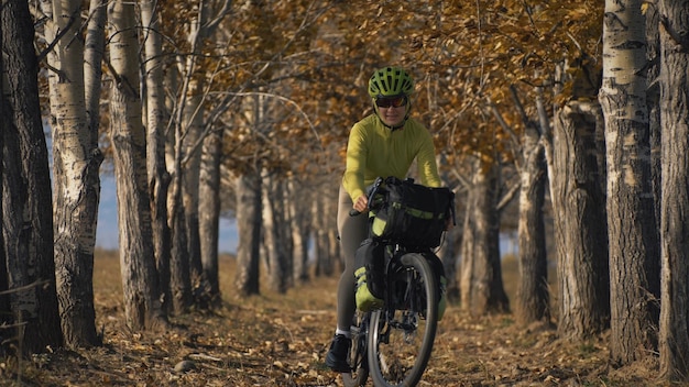 De vrouw reist op gemengd terrein fietstochten met bikepacking de reis van de reiziger met fietstassen sportkleding in groen zwarte kleuren de reis in het magische herfstbos arch alley avenue