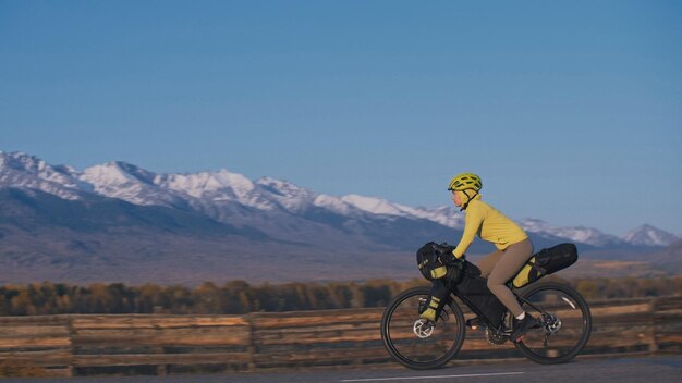 De vrouw reist op gemengd terrein fietstochten met bikepacking De reiziger reis met fietstassen Sporttoerisme bikepacking fiets sportkleding in groen zwarte kleuren Berg besneeuwde toppen