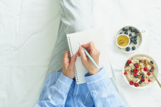 De vrouw schrijft in groot wit open notitieboekje, op bed ligt