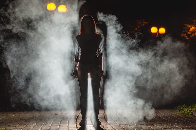 De vrouw staat op de rokerige straat. nachttijd