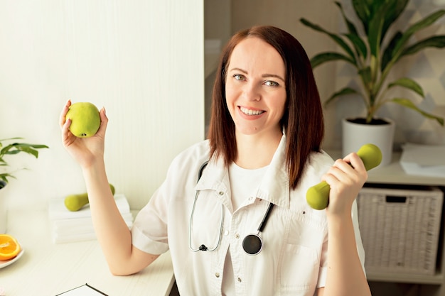 De vrouw van de artsenvoedingsdeskundige aan het werk met een in hand appel en kettlebell