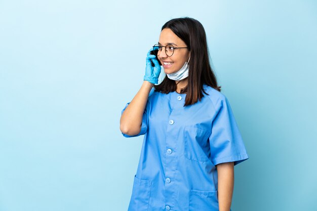 De vrouw van de chirurg over blauwe muur die een gesprek met de mobiele telefoon houdt