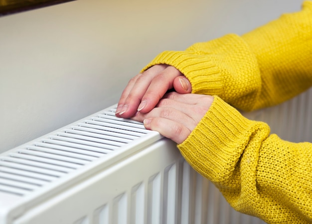 De vrouw verwarmt haar handen aan de radiator