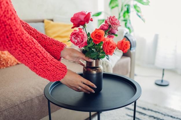 De vrouw zet vaas met bloemenrozen op lijst, Huisvrouw die gezelligheid in flat behandelen