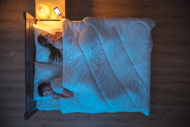 De vrouw zette de wekker op het bed naast de man. nacht tijd. uitzicht van boven