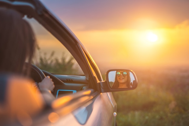 De vrouw zit in een auto op de achtergrond van de zonsondergang