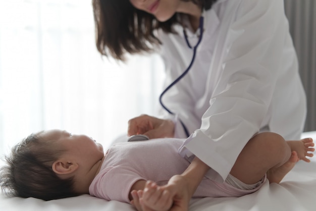 De vrouwelijke arts luistert de hartslag van het hart van leuke pasgeboren baby op het bed door stethoscoop te gebruiken.