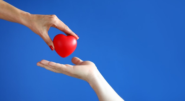 De vrouwelijke hand gaat rood hart over aan mannelijke hand tegen blauwe close-up als achtergrond.