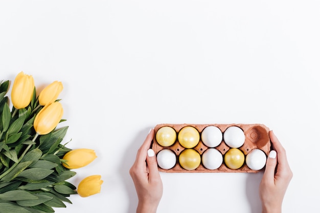 De vrouwelijke hand zet op de lijst een dienblad van paaseieren naast de gele tulpen