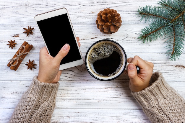 De vrouwelijke koffie en smartphone van de holdingskop en Kerstmisdecoratie op hout