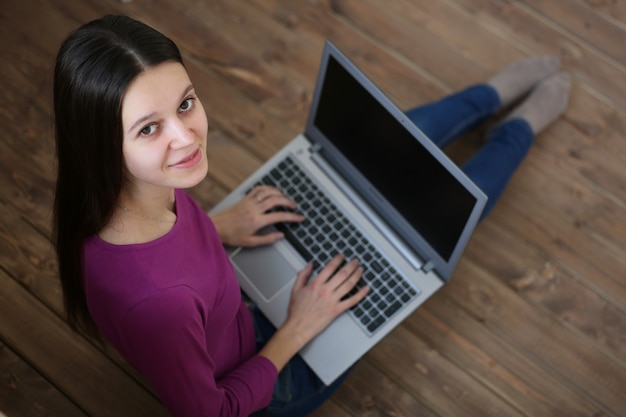 De vrouwelijke studentenzitting op de vloer met laptop en leert