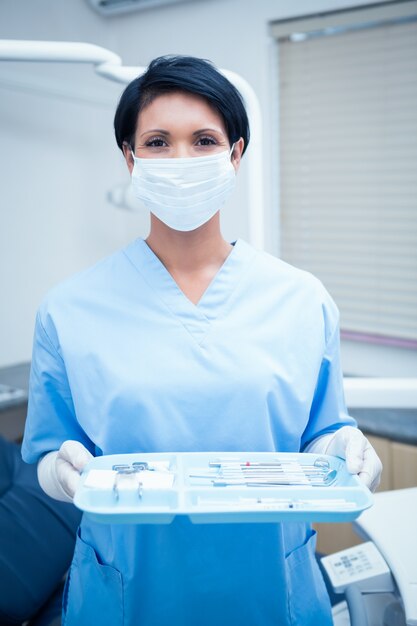 De vrouwelijke tandarts in blauw schrobt holding dienblad van hulpmiddelen