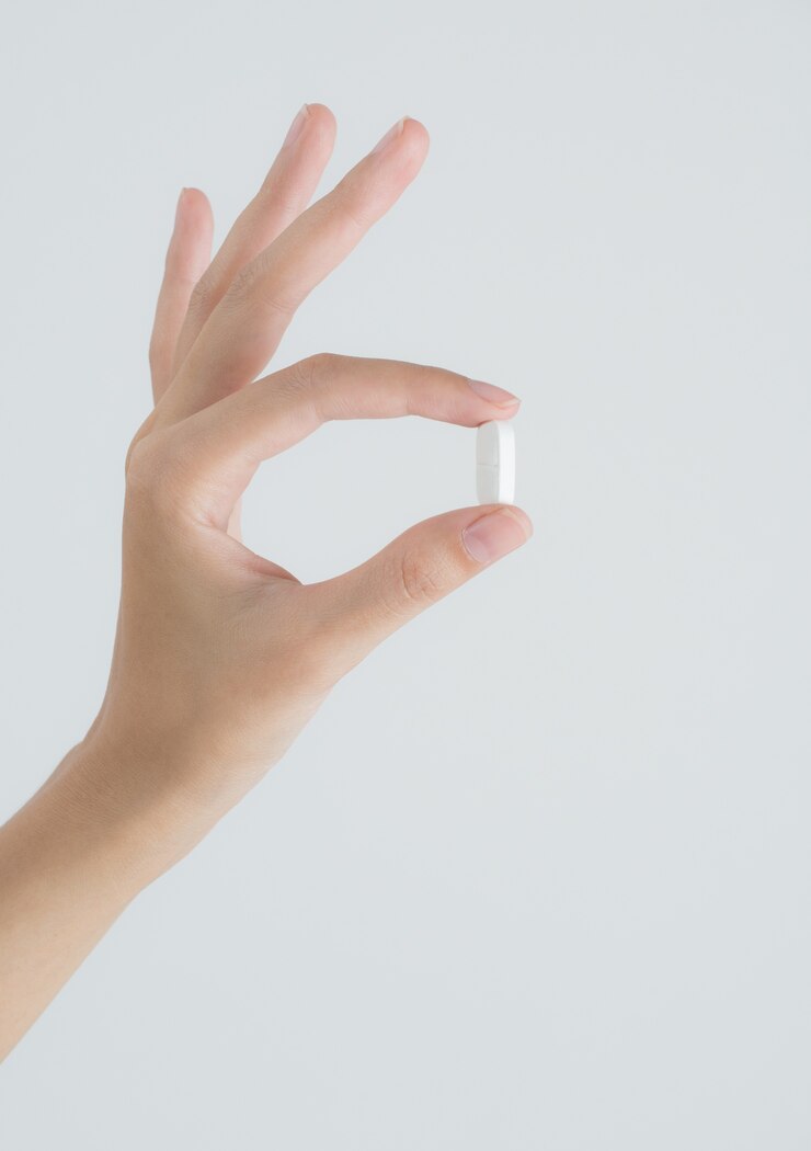 De vrouwenhand die van de close-up witte pillen op witte achtergrond houdt.