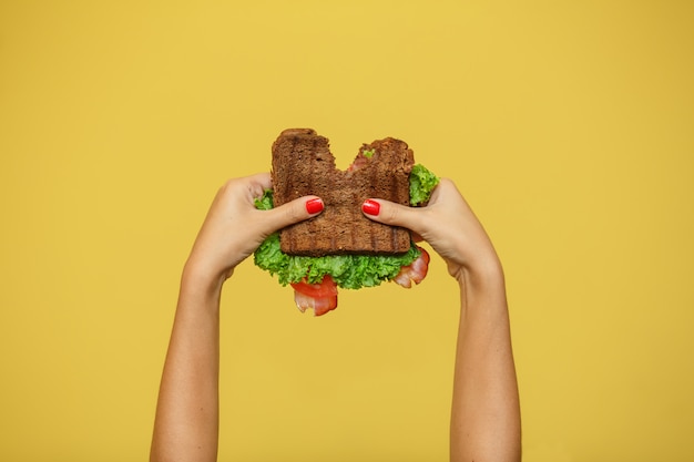 De vrouwenhanden houden gebeten sandwich op gele achtergrond. Sandwich promotie concept