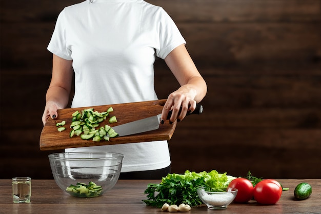 De vrouwenkok snijdt groenten voor saladevoorbereiding op hout.